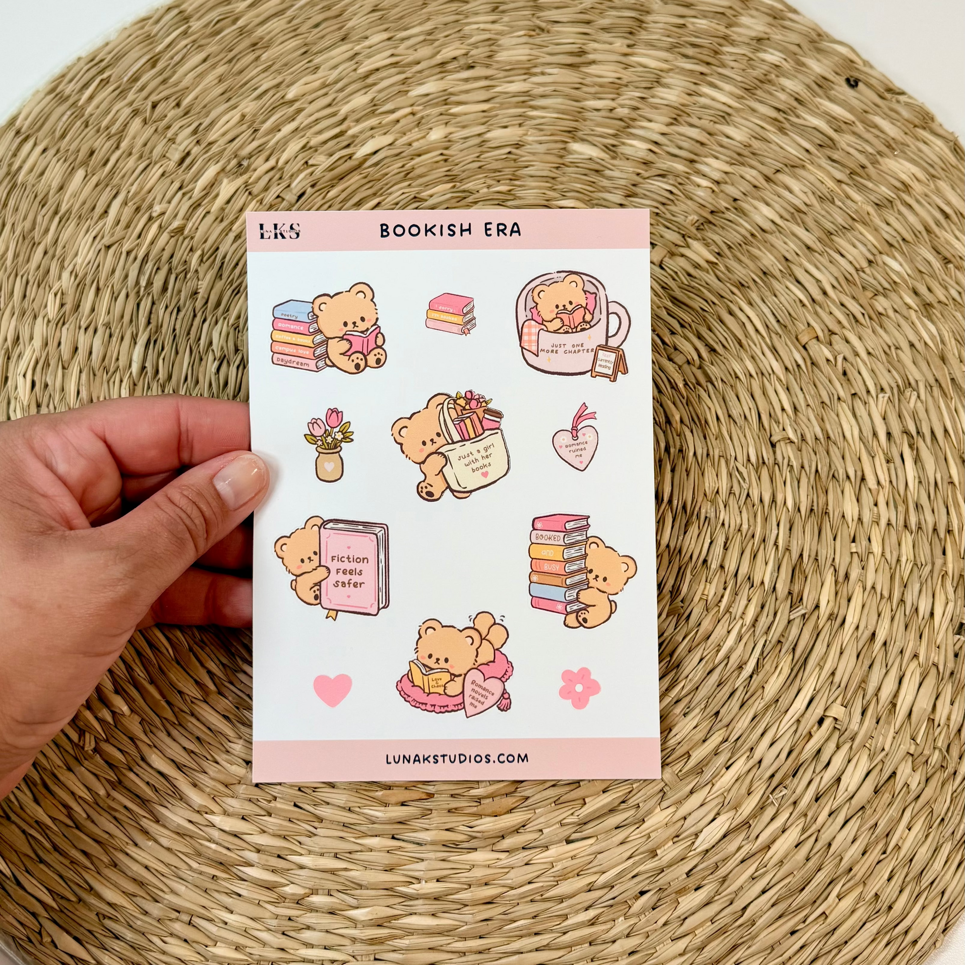 A hand holds a sheet of cute bookish-themed stickers against a white background with a round woven placemat underneath.