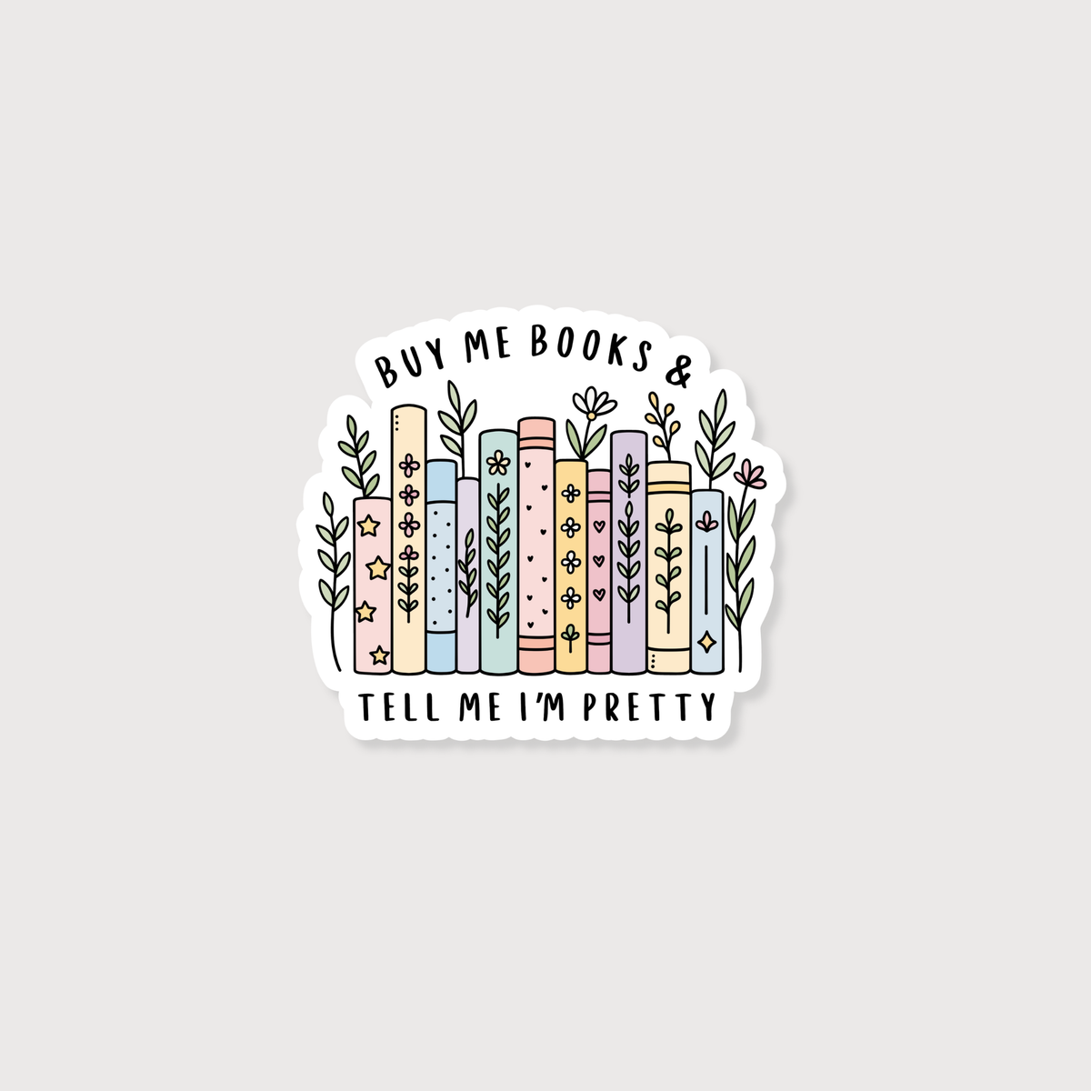 A die-cut sticker featuring a hand-drawn illustration of pastel-colored books with flowers and leaves, surrounded by the text 'BUY ME BOOKS & TELL ME I'M PRETTY' on a light gray background.
