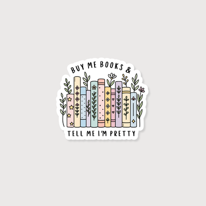 A die-cut sticker featuring a hand-drawn illustration of pastel-colored books with flowers and leaves, surrounded by the text 'BUY ME BOOKS & TELL ME I'M PRETTY' on a light gray background.