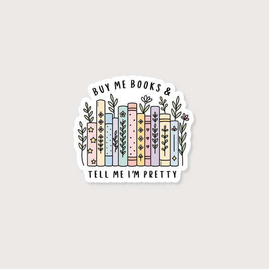 A die-cut sticker featuring a hand-drawn illustration of pastel-colored books with flowers and leaves, surrounded by the text 'BUY ME BOOKS & TELL ME I'M PRETTY' on a light gray background.