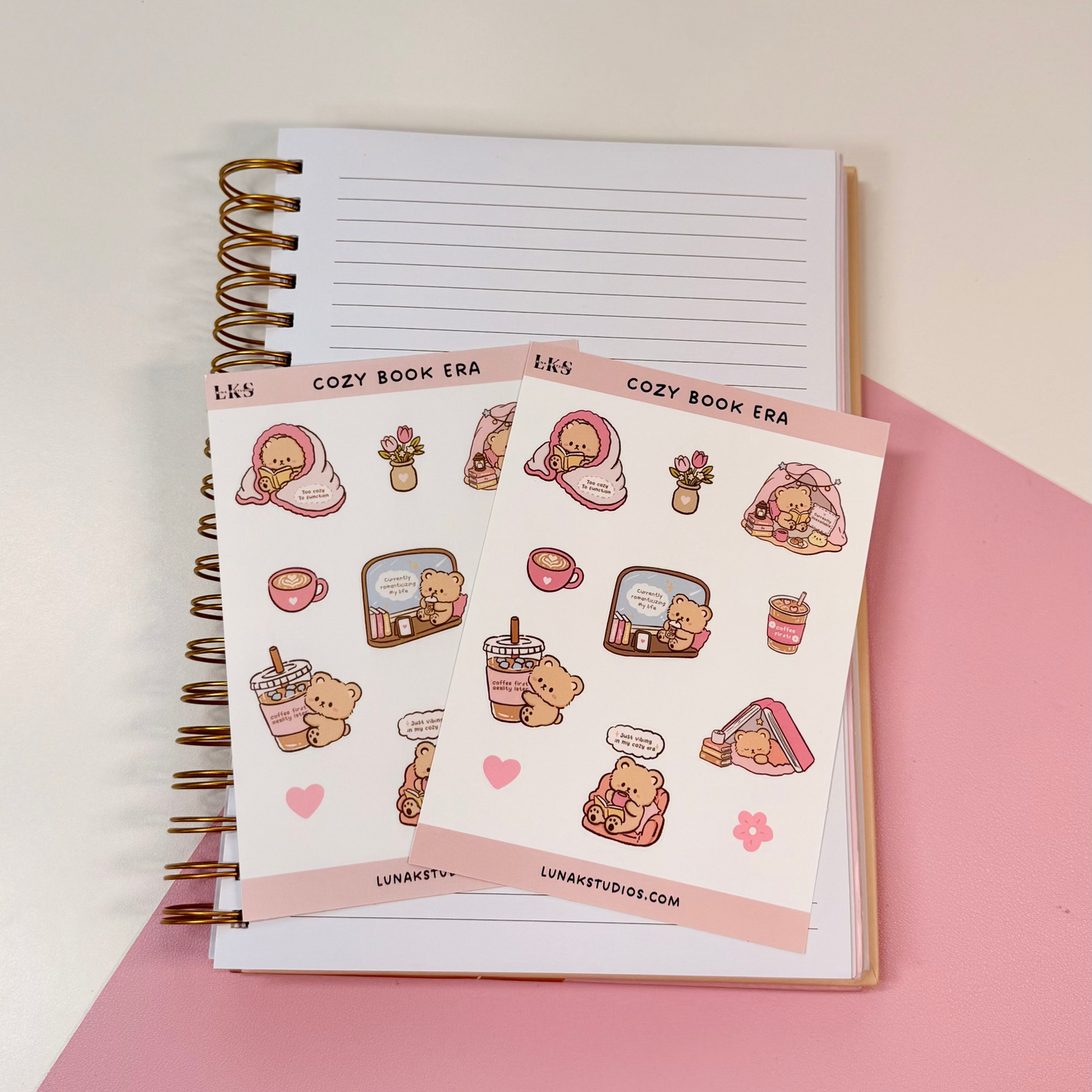 Two sheets of cute food-themed planner stickers displayed on top of an open lined spiral notebook, set against a split white and pink background.