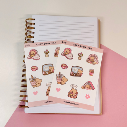 Two sheets of cute food-themed planner stickers displayed on top of an open lined spiral notebook, set against a split white and pink background.