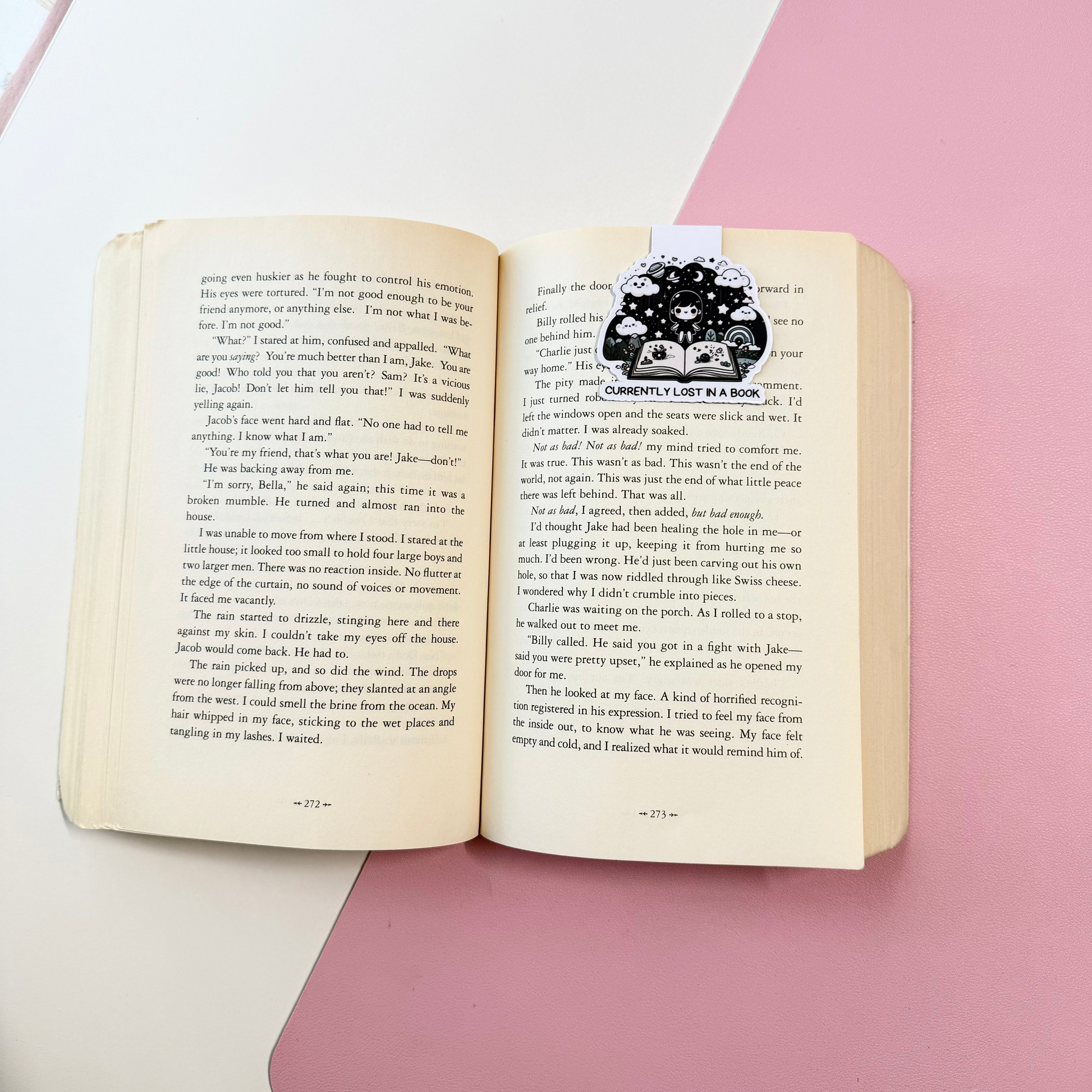 An open vintage book with printed text on both pages, featuring a black-and-white illustration. The book is placed on a pink and white geometric background.