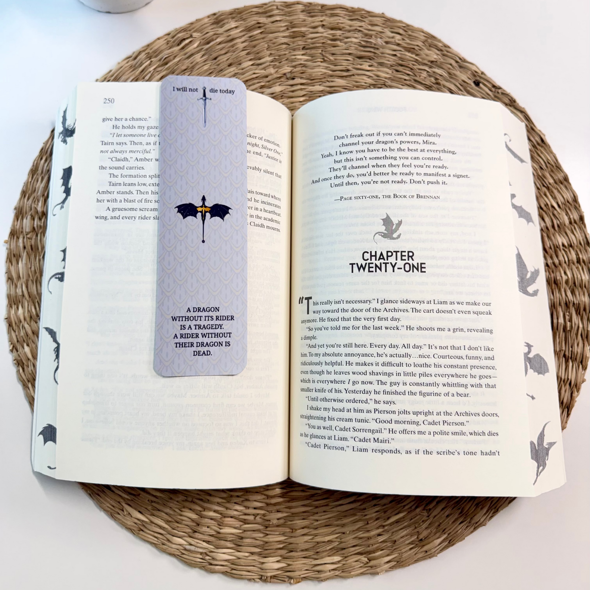 An open book on a woven round mat with a gray bookmark featuring a dragon illustration bookmark placed on the left page.
