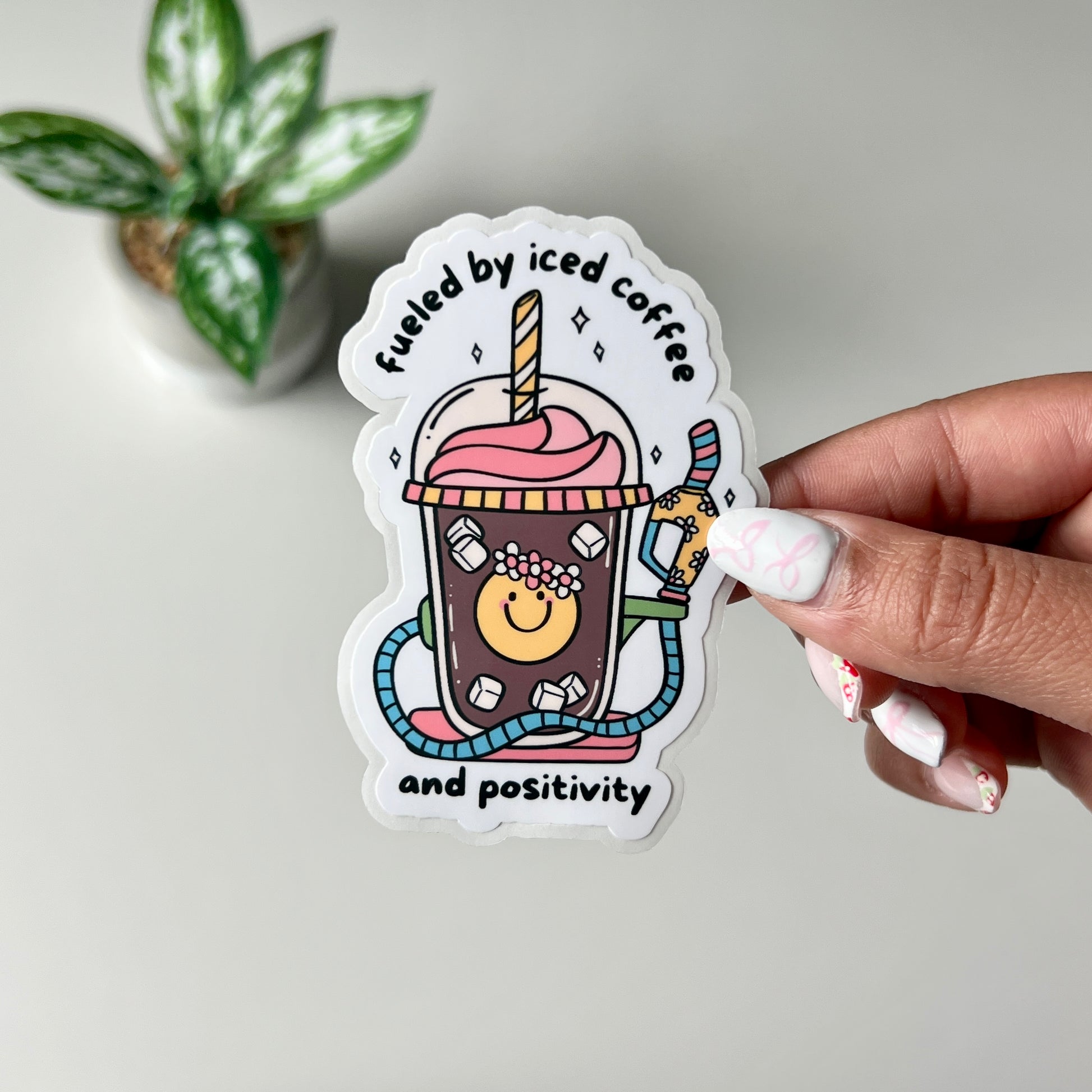 Iced coffee with a colorful gas pump handle with the words Fueled By Iced Coffee And Positivity being held by a hand