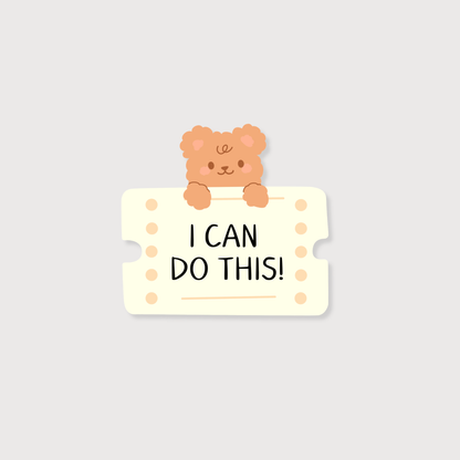 A cute cartoon sticker or decal featuring a small peach-colored teddy bear peeking over a cream ticket-shaped sign with the text 'I CAN DO THIS!' in black uppercase letters, set against a solid light gray background.