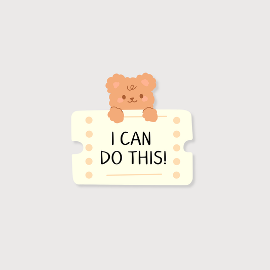 A cute cartoon sticker or decal featuring a small peach-colored teddy bear peeking over a cream ticket-shaped sign with the text 'I CAN DO THIS!' in black uppercase letters, set against a solid light gray background.