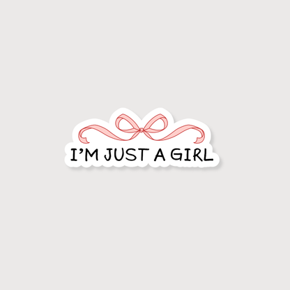 A die-cut sticker with the text 'I'M JUST A GIRL' in black lettering, underlined by a pink ribbon illustration, on a light gray background.