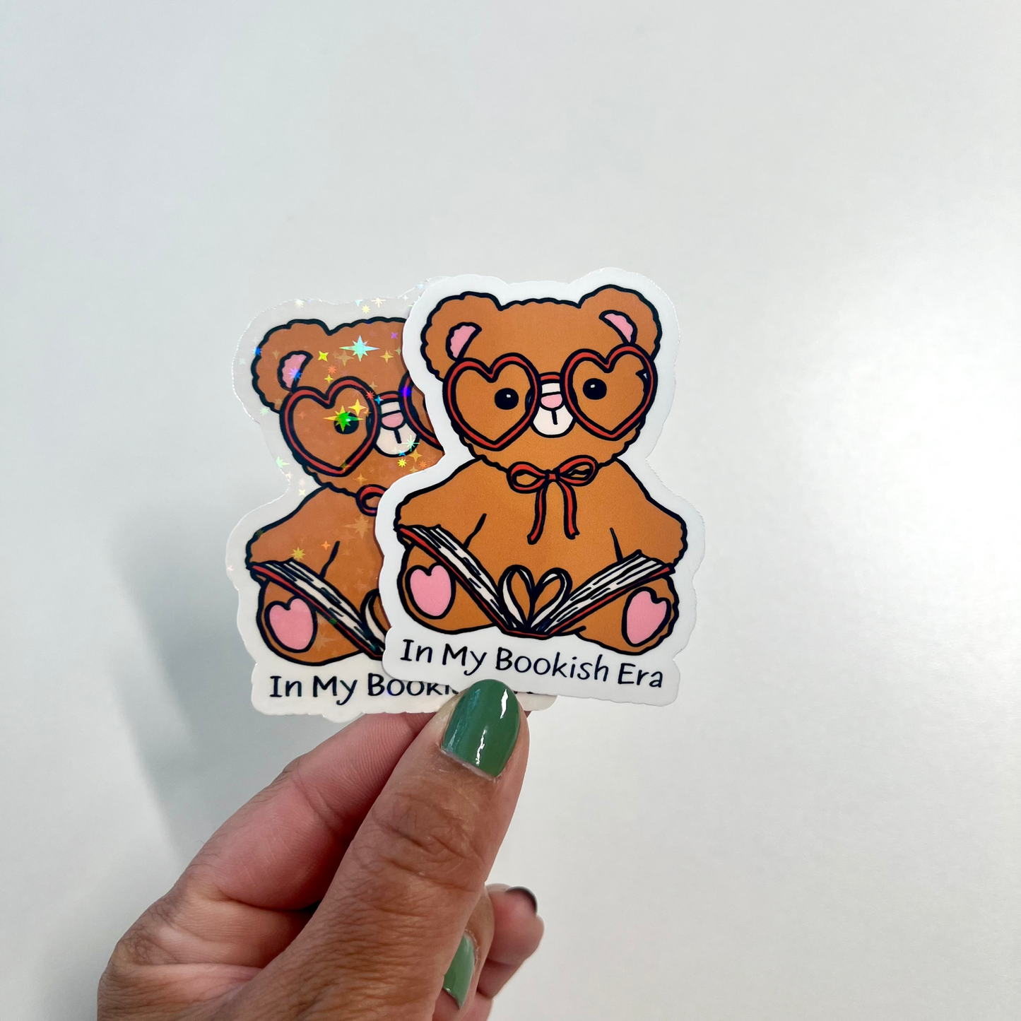 Sticker of two teddy bears with glasses held by a hand on a light gray background