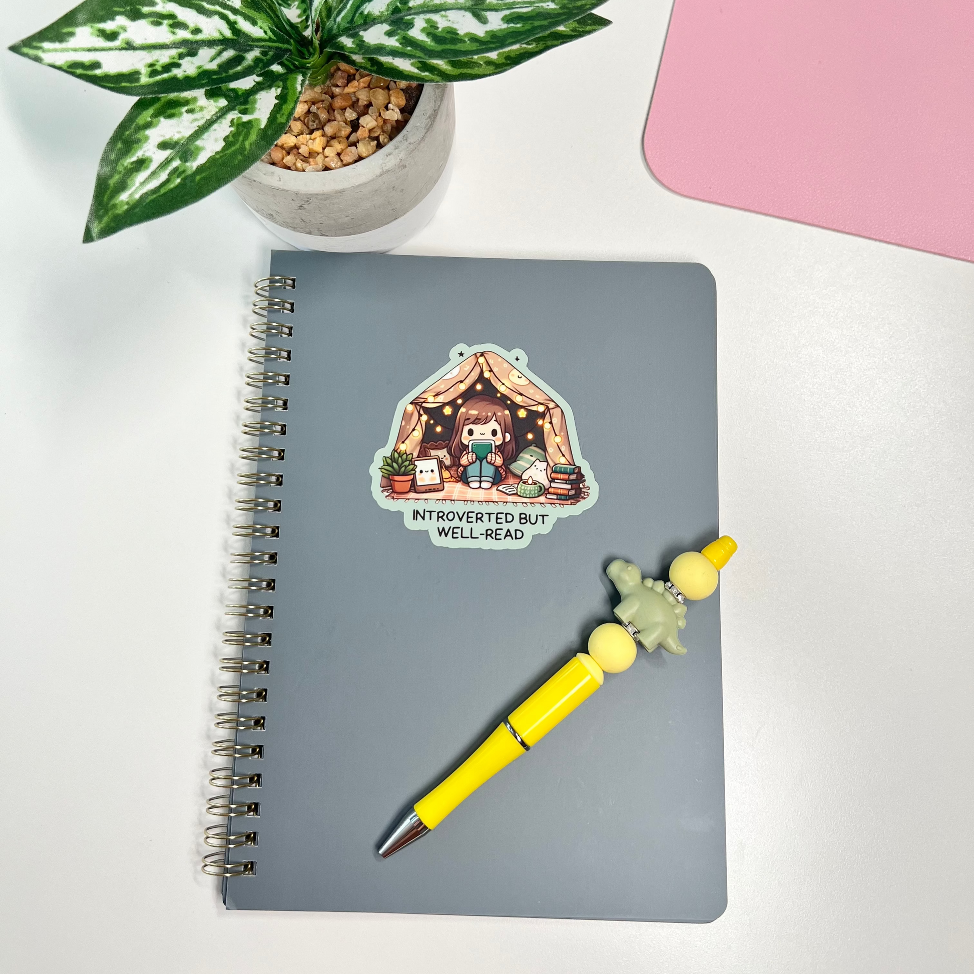 Notebook with a sticker, yellow pen, and plant on a white surface