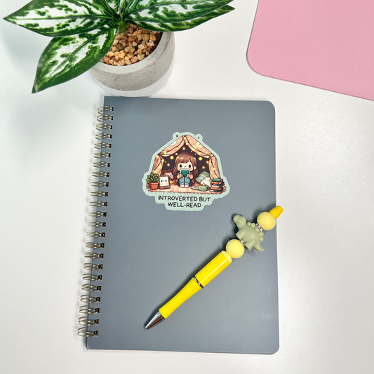 Notebook with a sticker, yellow pen, and plant on a white surface