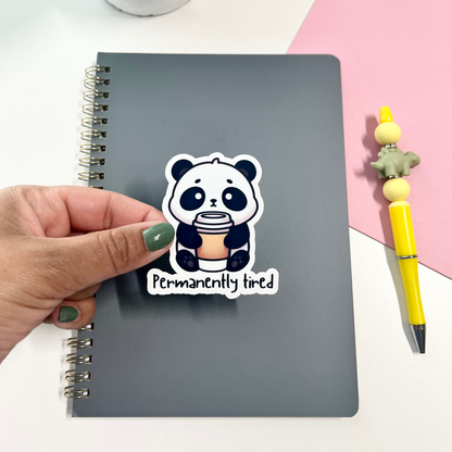 Hand holding a sticker with a panda design on a notebook with a pink and white background.
