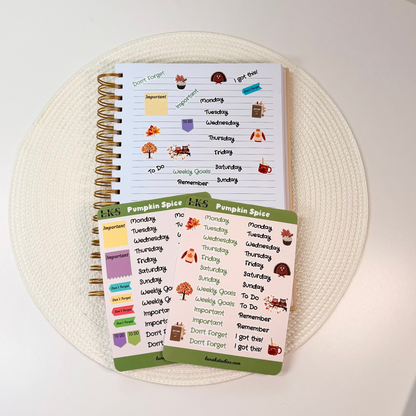 A spiral-bound planner and matching sticker sheets with autumn-themed labels, arranged on a round woven placemat on a white tabletop.