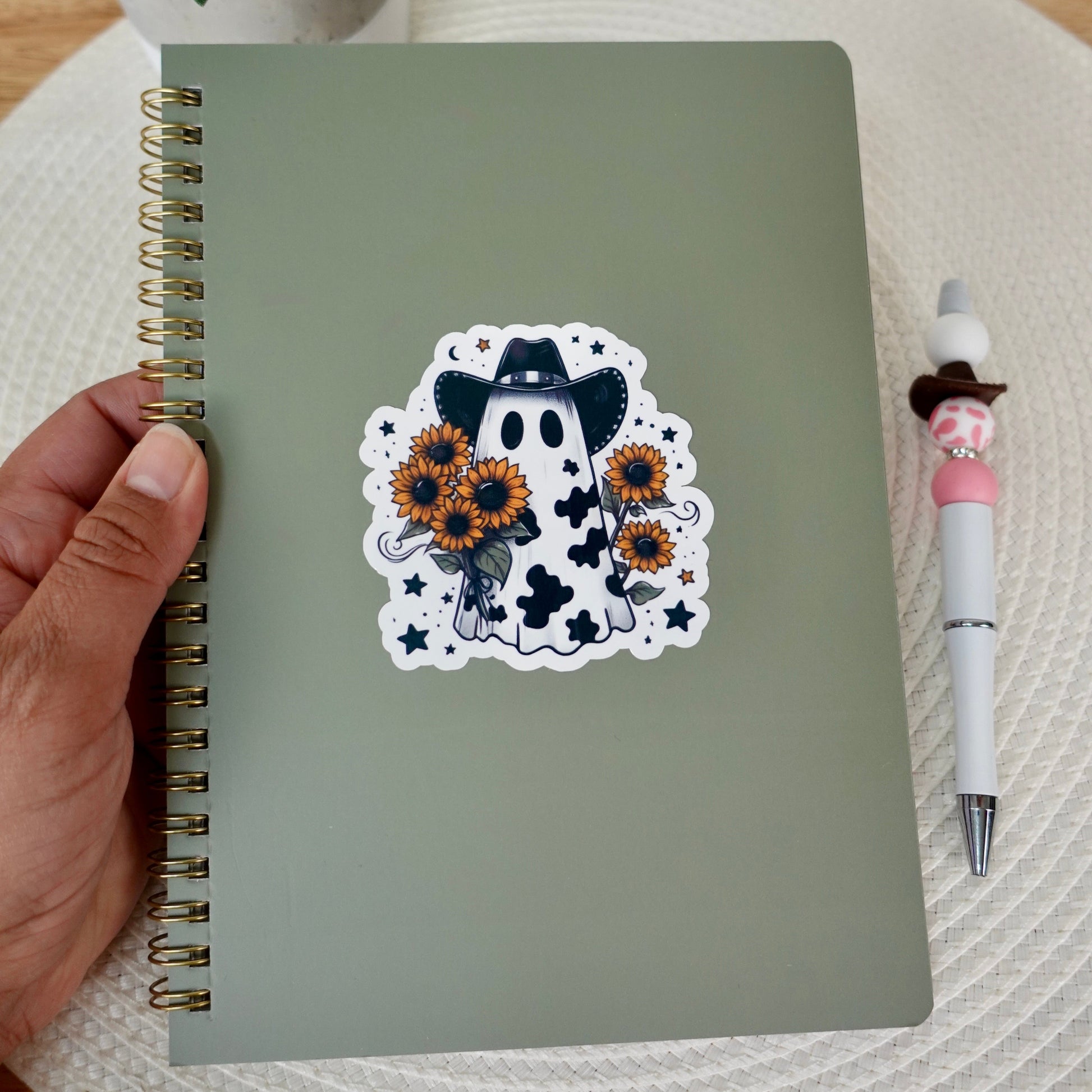 Black cow print ghost with cowboy hat holding sunflowers on a notebook