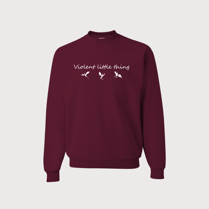 A maroon crewneck sweatshirt with 'Violent little thing' and two small bird silhouettes printed in white across the chest, displayed on a light gray background.